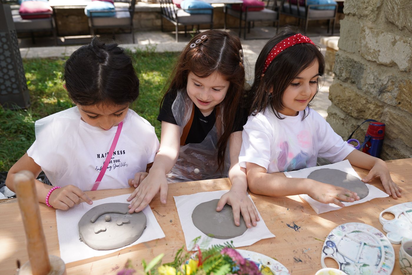 Three girls working with clay at an outdoor table on a sunny day