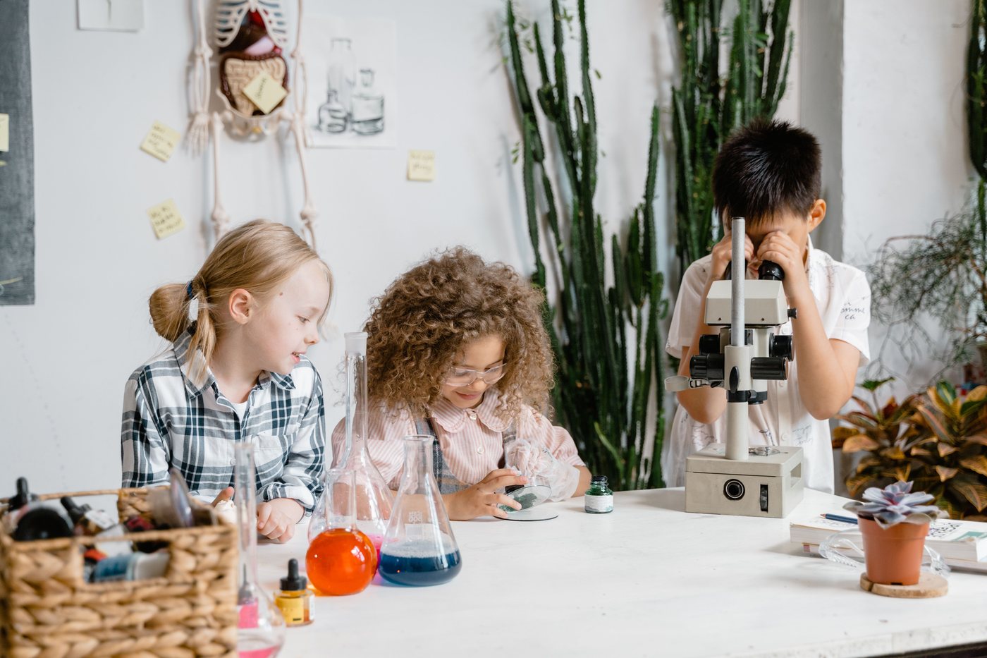 Three children work at a science table; one looks through a microscope