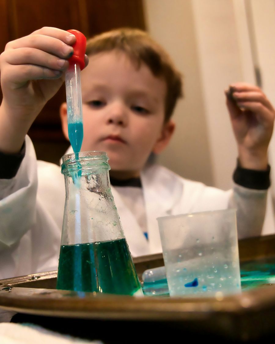 A boy in a lab coat squeezes a dropper over a flask