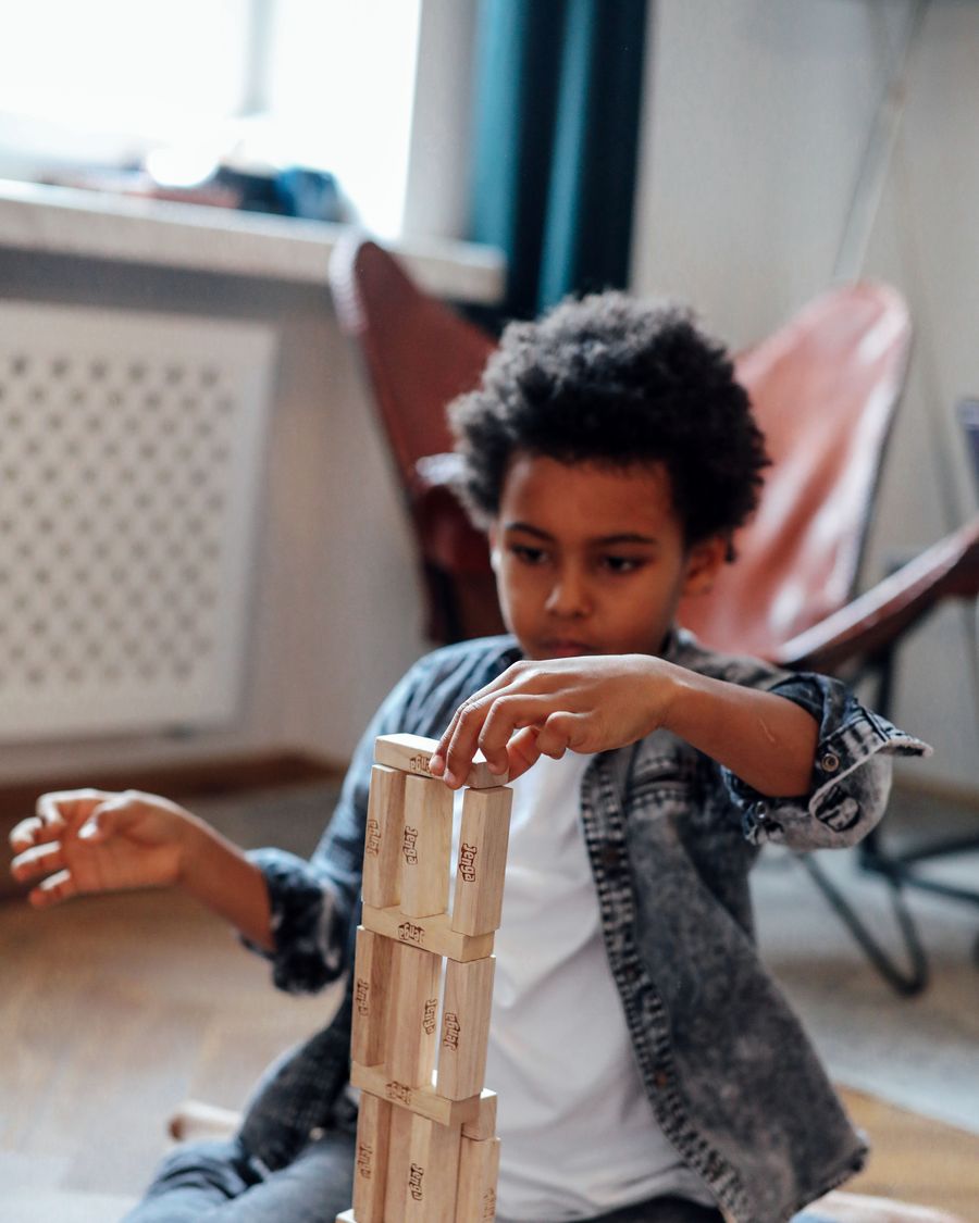 A boy balances a tall tower of wooden blocks