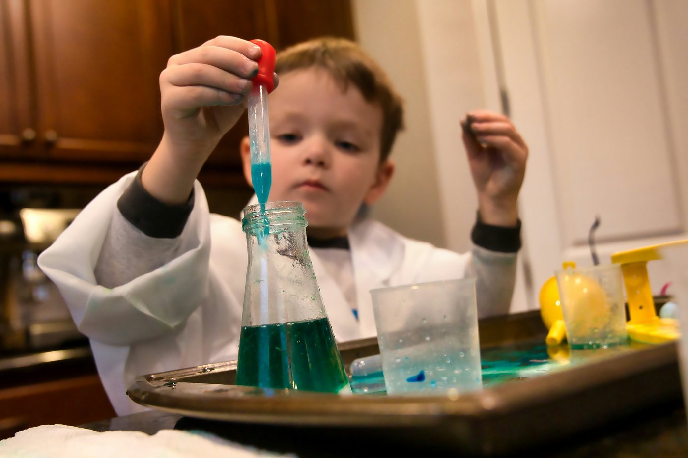 A boy in a lab coat squeezes a dropper over a flask