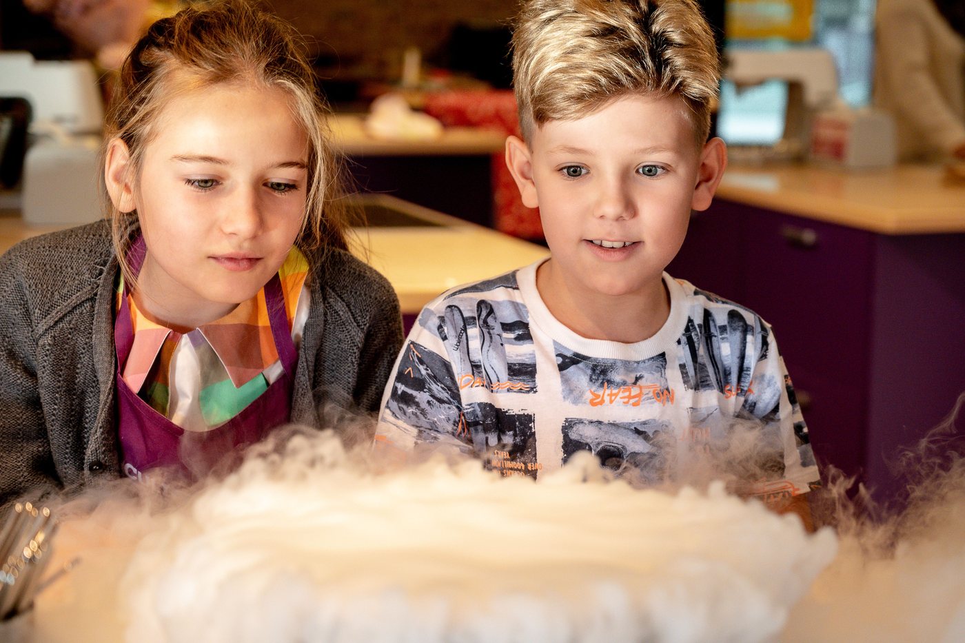 A girl and a boy lean in to watch fog pour over a table during a science demonstration