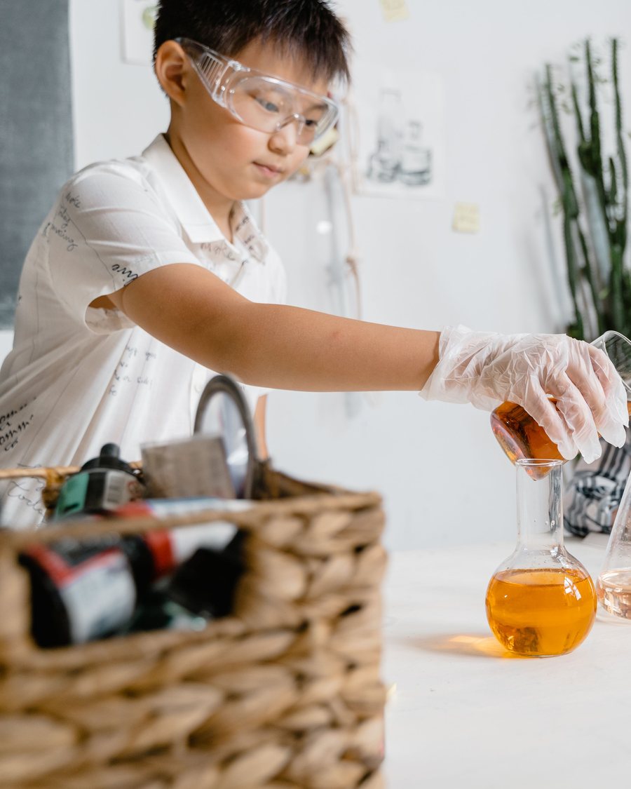 A boy in safety glasses carefully pours liquid into a flask